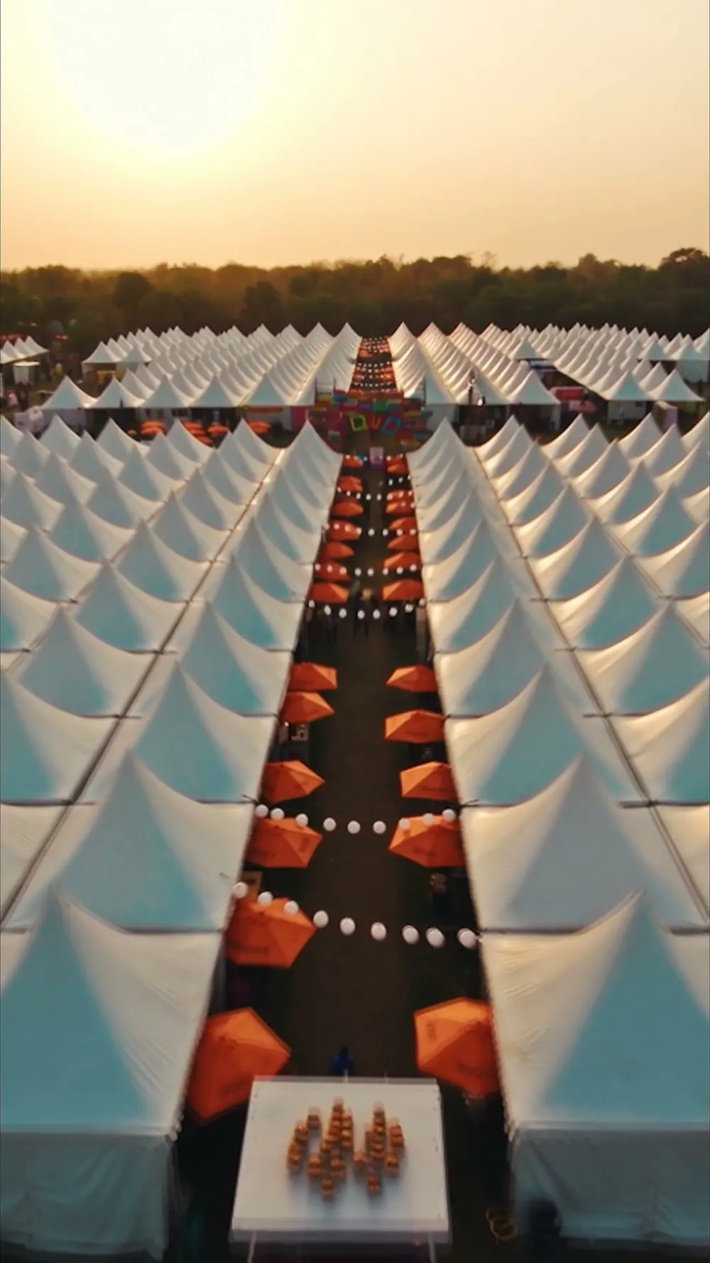 Aerial view of two long rows of white stall canopies with orange umbrellas at sunset