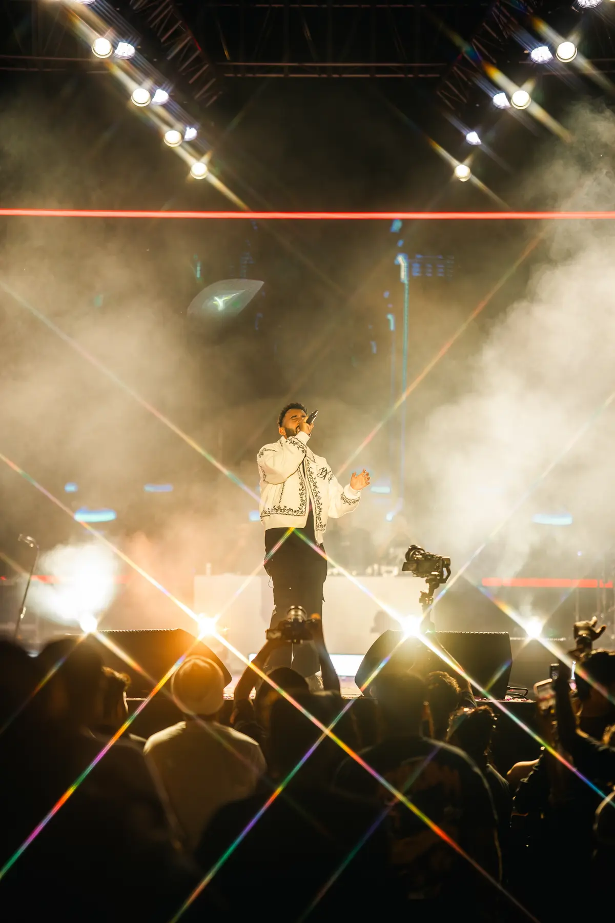 A performer in a white jacket under star-burst spotlights